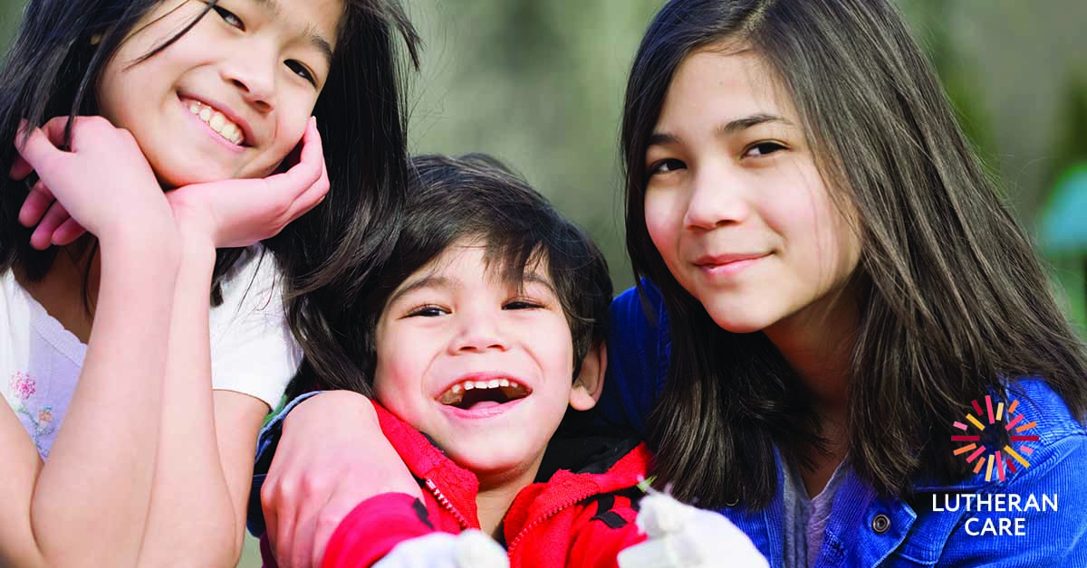 Three siblings art sitting together smilling and laughing at the camera. The Lutheran Care logo appears in the bottom right hand corner.