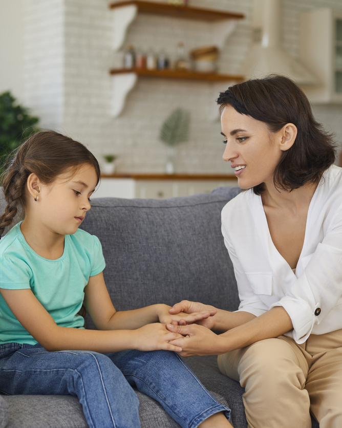 Sad young girl talking with her mum on a couch at home.